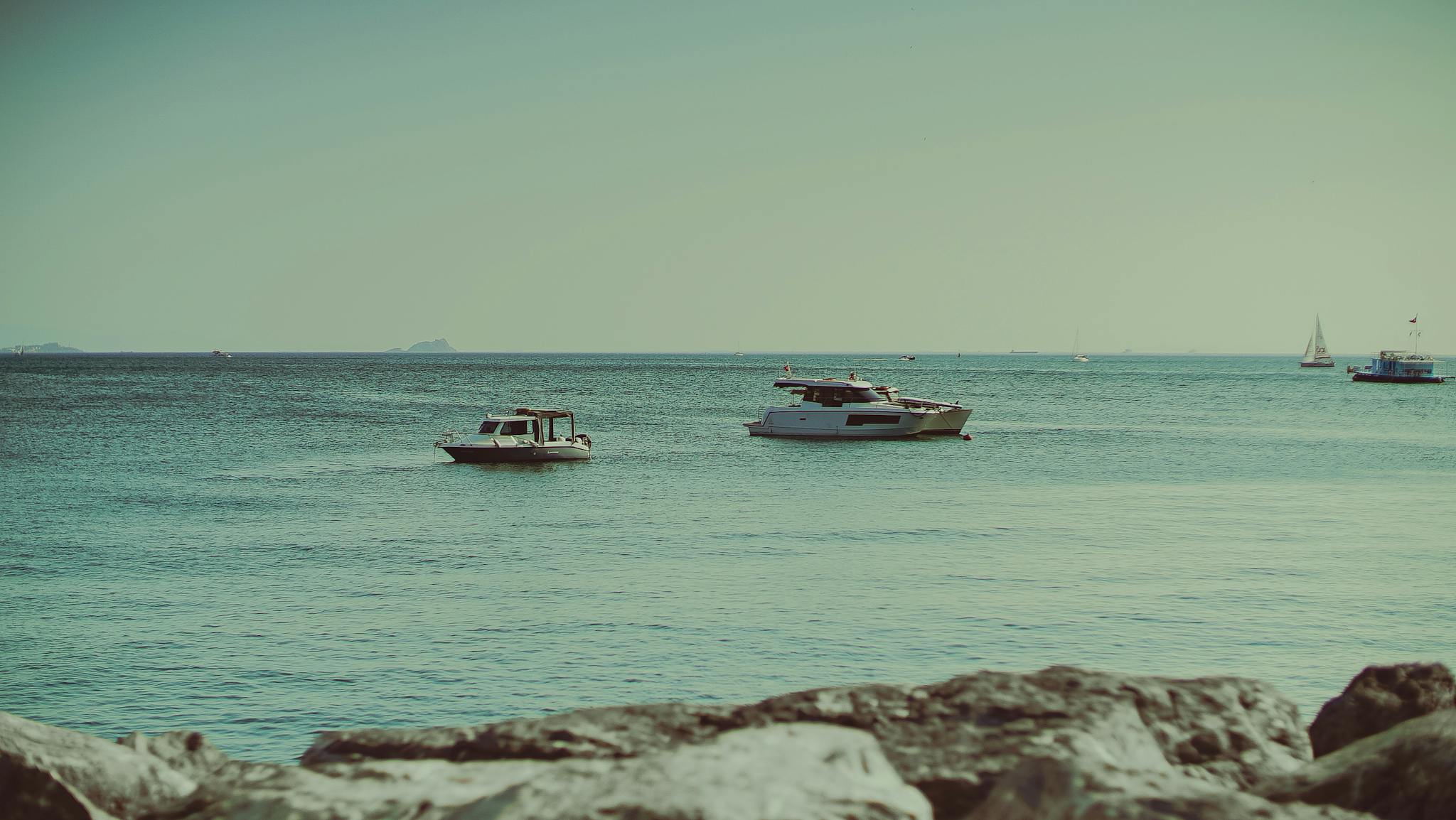 Boats floating in calm sea near rocky shore with clear skies.